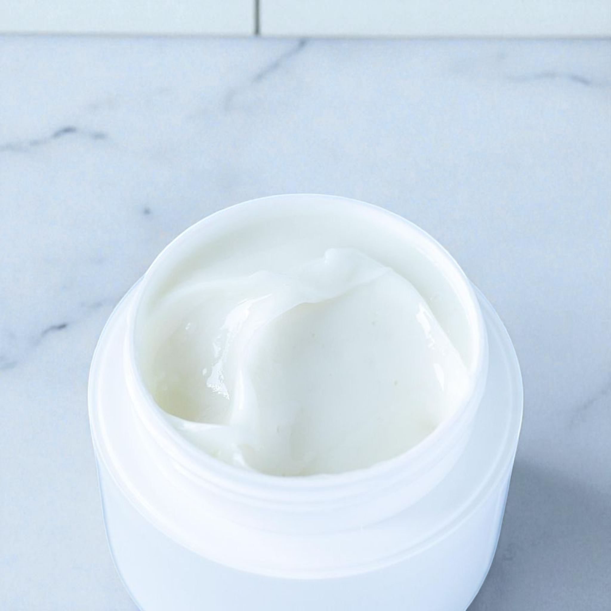 White jar of lotion on a white marble background